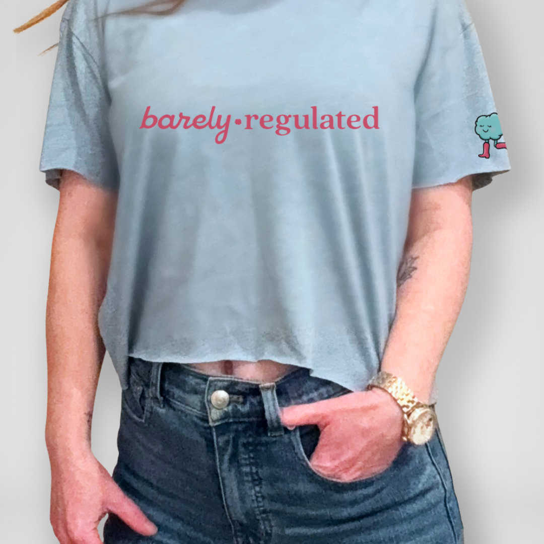 Person wearing a light blue t-shirt with 'barely regulated' text and jeans against a plain background