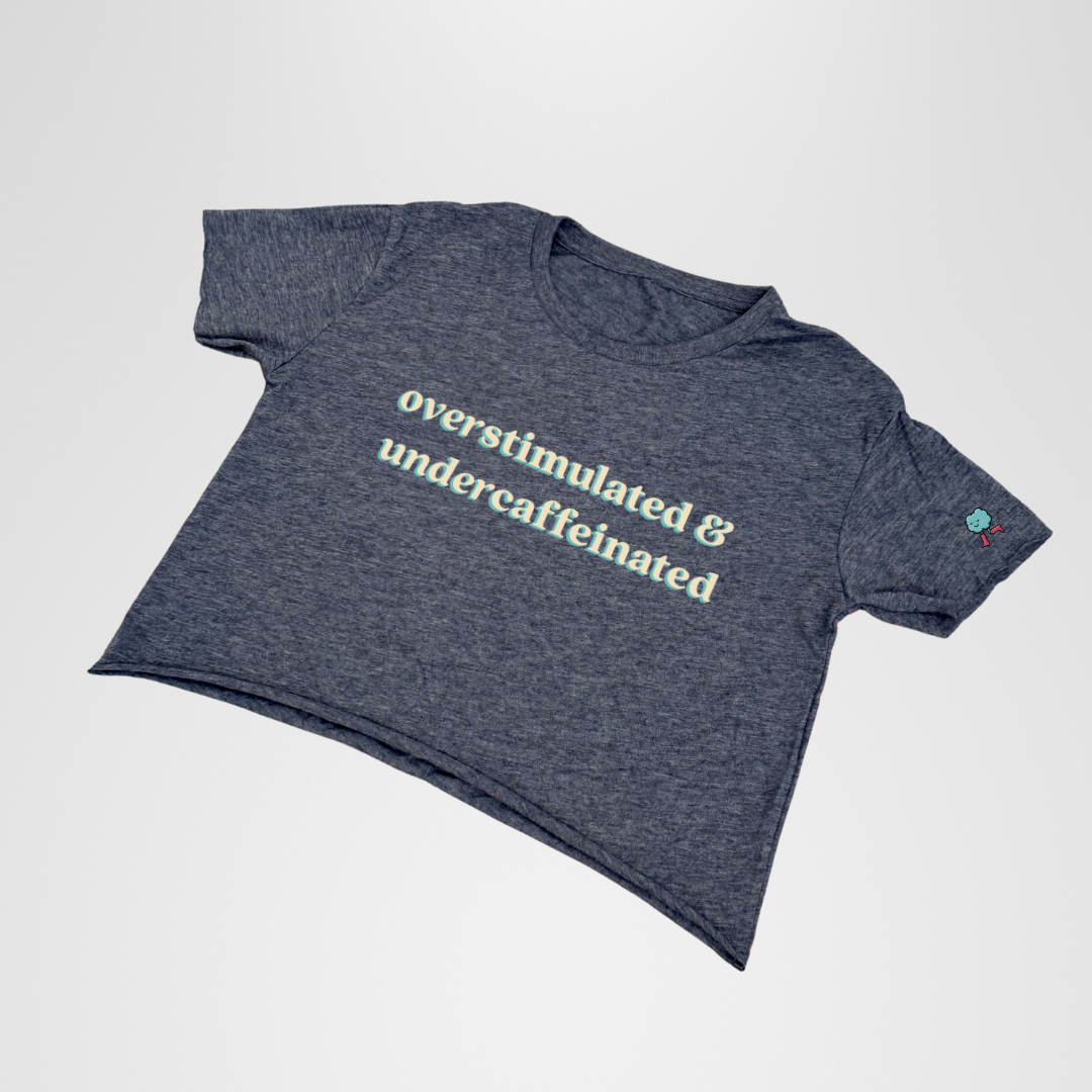 Gray t-shirt with text 'overstimulated & undercaffeinated' on a light gray background