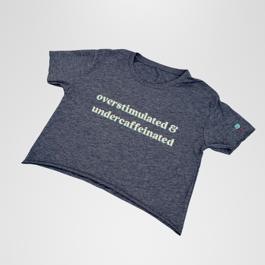 Gray t-shirt with text 'overstimulated & undercaffeinated' on a light gray background