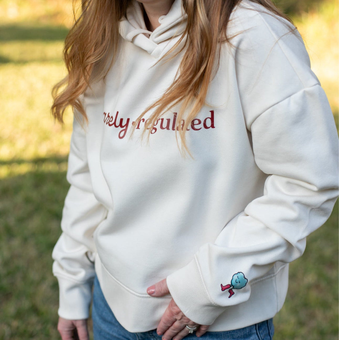 Woman wearing a cream hoodie with 'Barely Regulated' text outdoors
