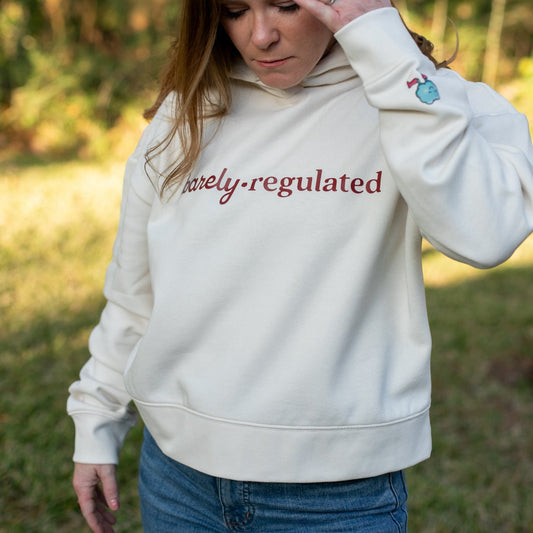 Person wearing a cream hoodie with 'Barely Regulated' text outdoors