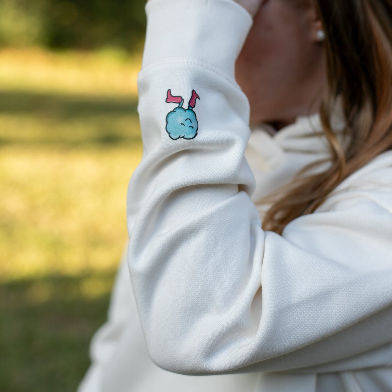 Person wearing a cream sweatshirt with a cloud design outdoors