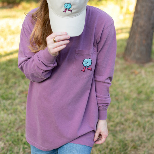 Person wearing a purple long-sleeve shirt with a cloud logo, holding a cream cap outdoors.